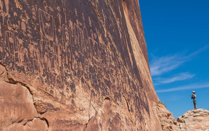 A person appears small as they stand beside a very steep and tall canyon wall.